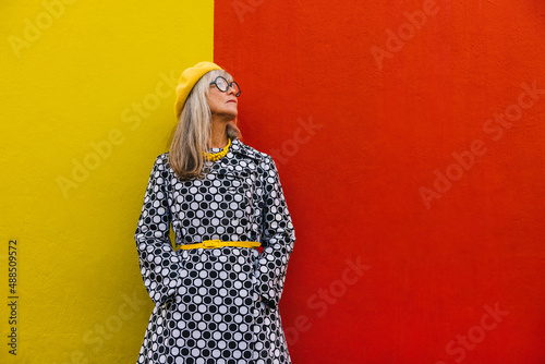 Elderly woman looking away thoughtfully against a colourful wall