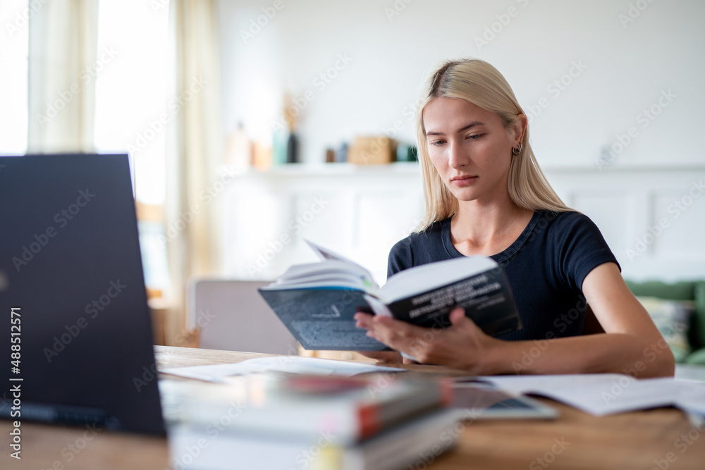 Woman student reading book sitting at table Woman student reading book sitting at table