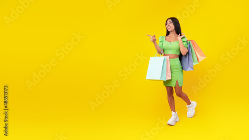 Young lady walking with bags at yellow studio background