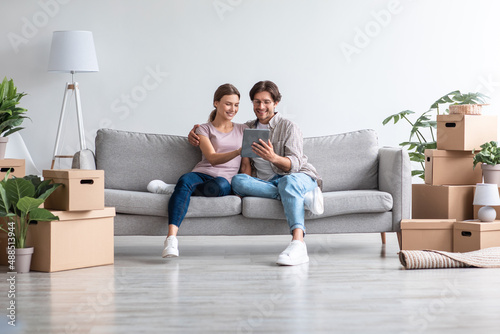 Satisfied young caucasian guy in glasses and lady in casual sit on sofa with tablet, planning new interior