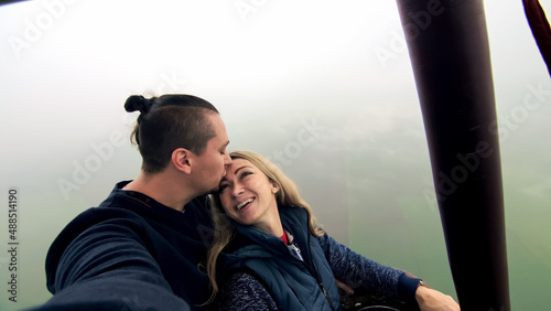 Adventure love couple on hot air balloon watermelon. Man and woman kiss hug love each other. Burner directing flame into envelope. Fly in morning blue sky. Happy people take selfie in hot air ballon.