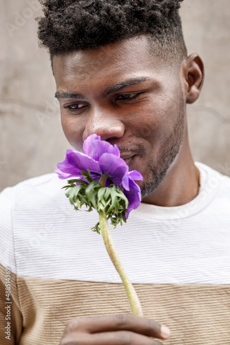 Portrait of a smiling young African American man smelling a purple flower on a brown background photo