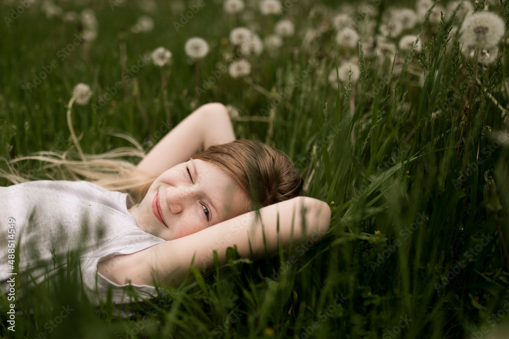 Cute girl winking and lying on dandelions in field Cute girl winking and lying on dandelions in field