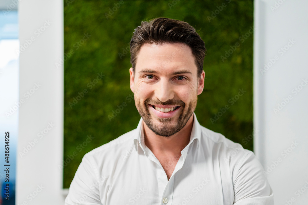 Happy businessman in front of wall at office