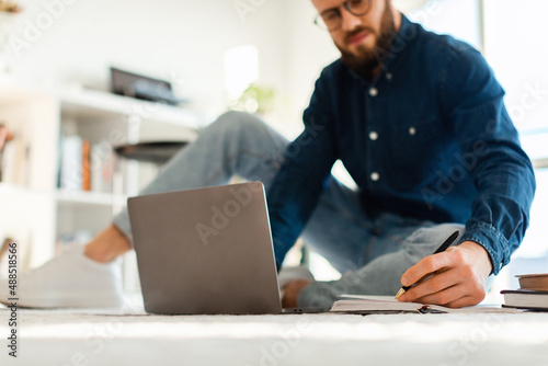 Man Taking Notes Using Laptop Sitting On Floor Indoors, Cropped
