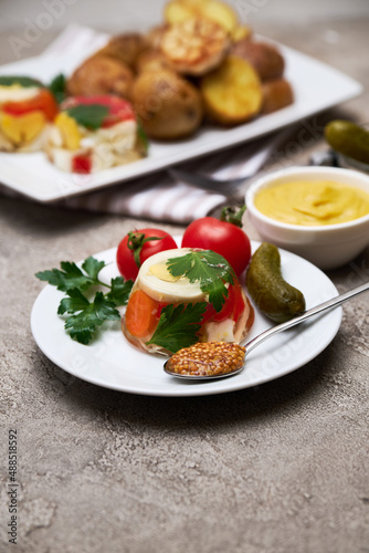 Portion of delicious chicken aspic and baked potato on a plate on concrete table