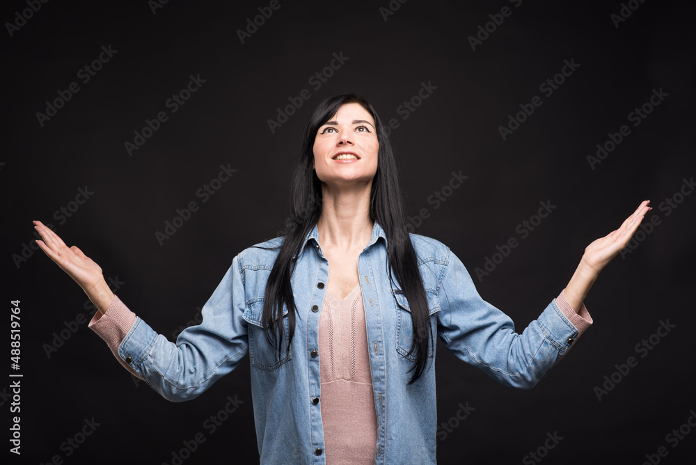 Attractive caucasian brunette girl in shirt thanking god for good luck isolated on black studio background. Attractive caucasian brunette girl in shirt thanking god for good luck isolated on black studio background.