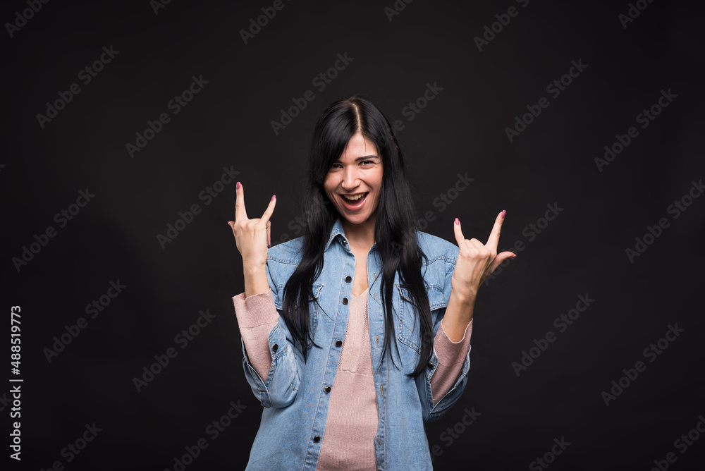 Attractive caucasian brunette girl in shirt happily screaming and showing rocker or punk gesture isolated on black studio background. Attractive caucasian brunette girl in shirt happily screaming and showing rocker or punk gesture isolated on black studio background.