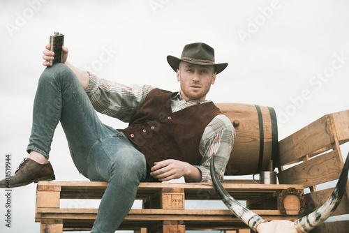 American cowboy man. Handsome brutal western guy. Attractive man with whiskey or brandy.