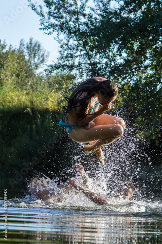 Fototapeta Naklejka Na Ścianę i Meble -  young girl jumping into the river in the summer on a hot day