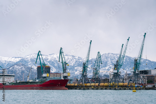 Close-up of a container ship, port cranes in the commercial port of Batumi against the background of the snow-capped Caucasus mountains