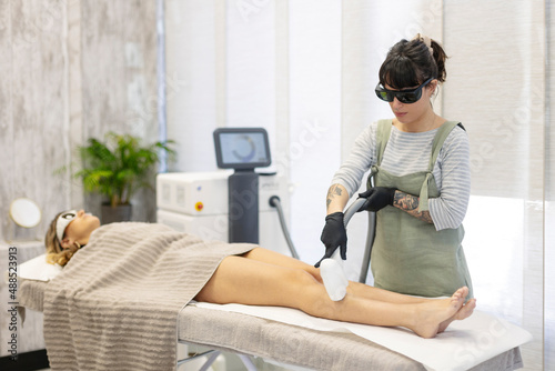 Beautician using hair removal laser machine on woman at aesthetic clinic