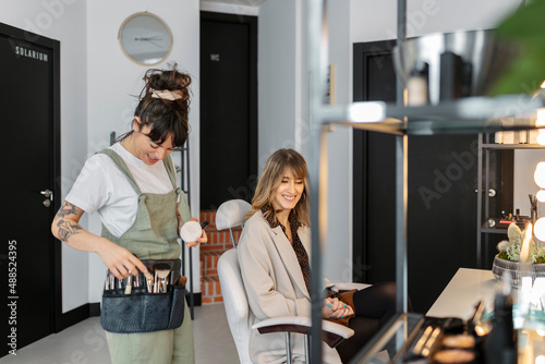 Happy make-up artist talking with customer sitting on chair at salon