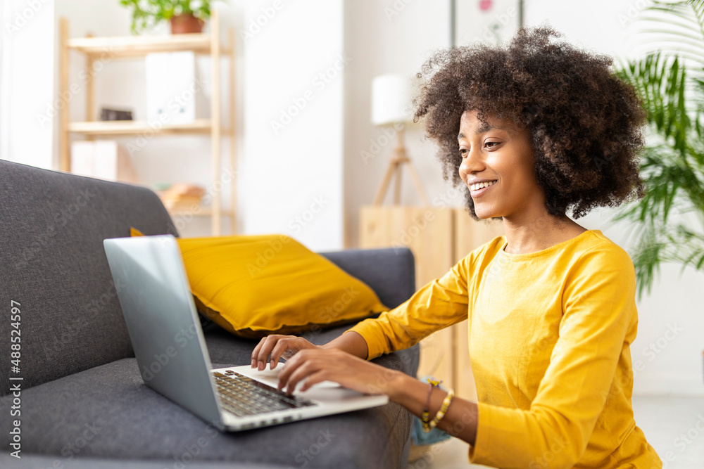 Happy young woman using laptop by sofa at home Happy young woman using laptop by sofa at home