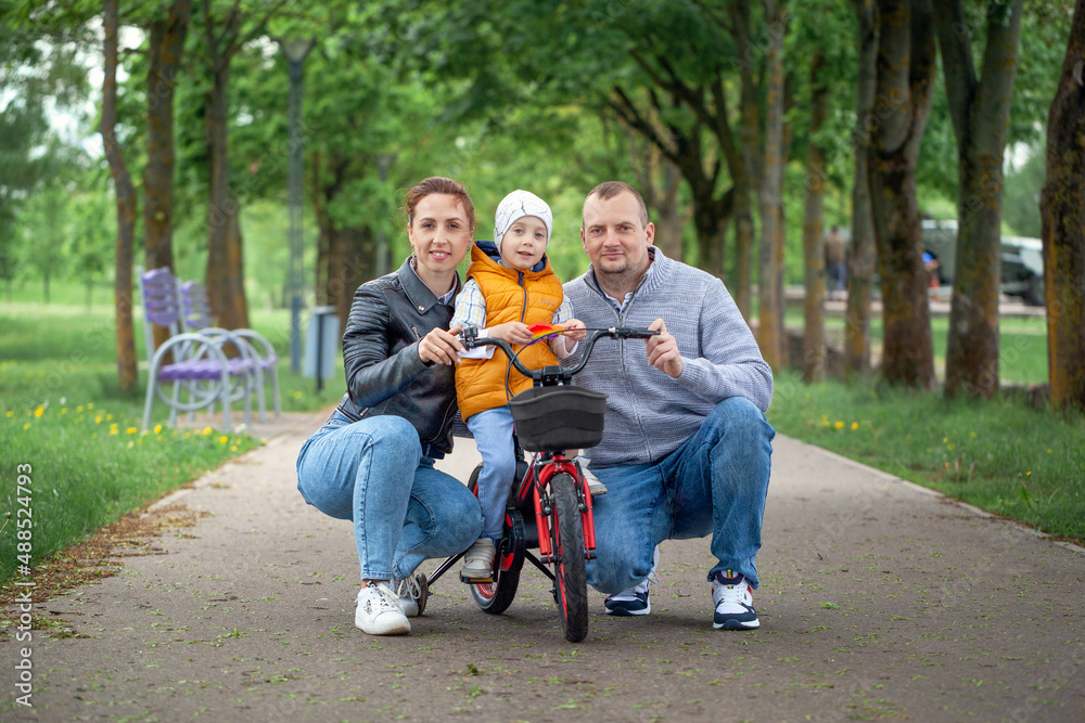 Happy family walking in the summer park. Child riding a bike Mom, dad and baby are happy to walk in summer day.