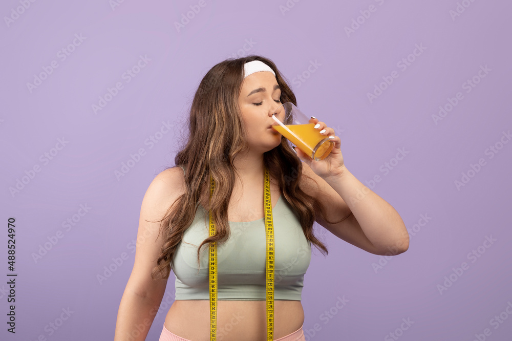 Calm pretty plus size young woman in sportswear with closed eyes and measuring tape drinking glass of orange juice Calm pretty plus size young woman in sportswear with closed eyes and measuring tape drinking glass of orange juice