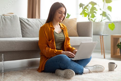 Slika na platnu Full length of happy young woman sitting cross legged on floor with laptop pc, w