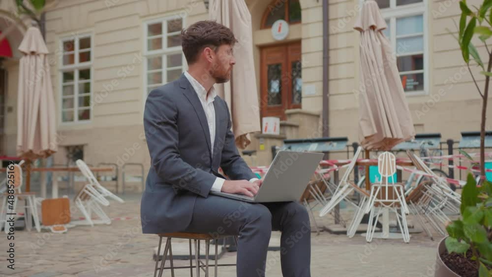 Frustrated unemployed caucasian business owner in suit sits with laptop on terrace of his restaurant in depressed state. Job dismissal. Crisis 2020. Business shutdown. Frustrated unemployed caucasian business owner in suit sits with laptop on terrace of his restaurant in depressed state. Job dismissal. Crisis 2020. Business shutdown.