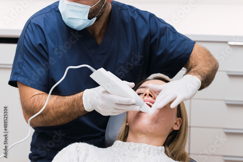 Dentist examining patient's teeth with intraoral scanner in clinic photo