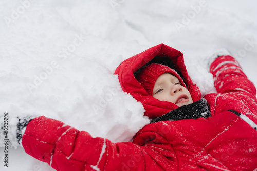 Boy wearing warm clothing lying on snow in winter photo