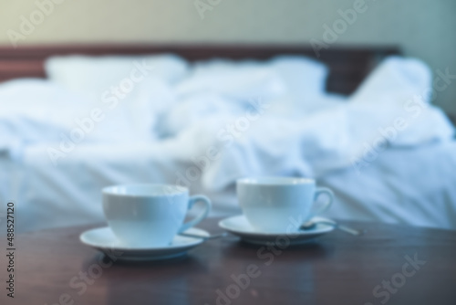 Blurred background room in the hotel with white cups on the table and bed with white bedding