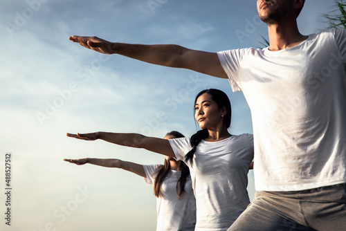 Group of people doing yoga exercises by the lake at sunset.