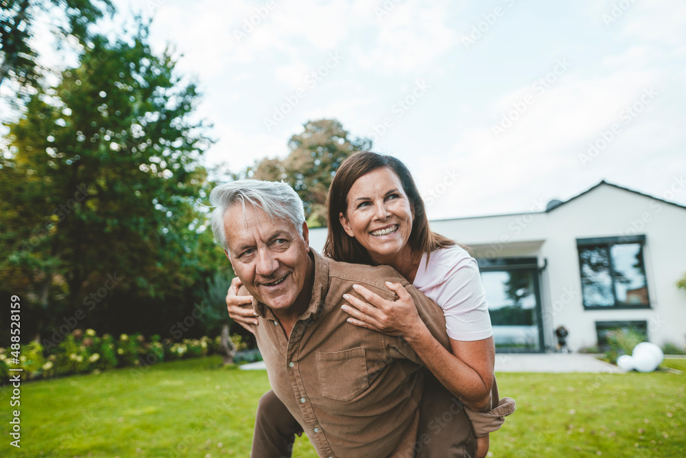Happy senior man giving piggyback ride to cheerful woman at backyard