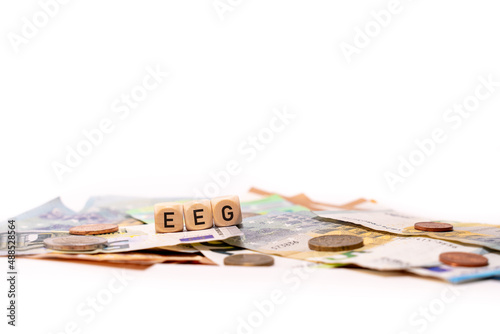 German word for Renewable Energies Act, EEG-UMLAGE, spelled with wooden letters wooden cube on a plain white background with banknotes and coins, concept image