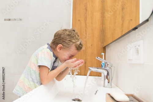 A five-year-old boy washes his hands in the bathroom. A boy of five years old, European outside washes his hands in the bathroom in front of the mirror