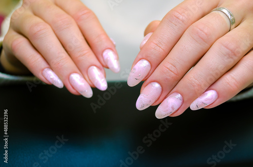 Close-up of beautiful female hands with a luxurious manicure  nails covered with pink gel polish with a design