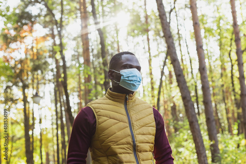 Handsome african american man wearing casual clothes and medical mask smiling happy walking in spring park