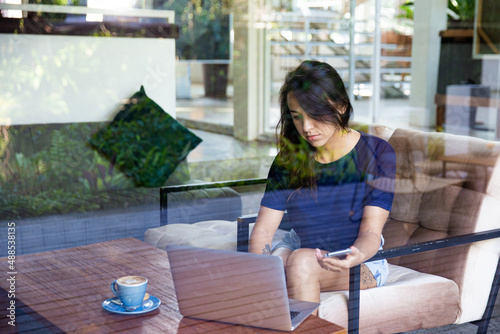 Young woman freelancer working remotly with laptop in cafe, she drinking cappuccino. photo