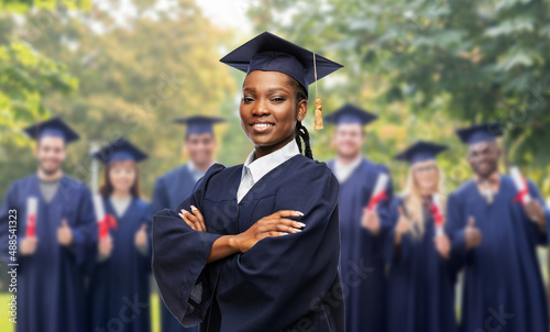 education, graduation and people concept - happy graduate student woman in mortarboard and bachelor gown over group of people on background photo