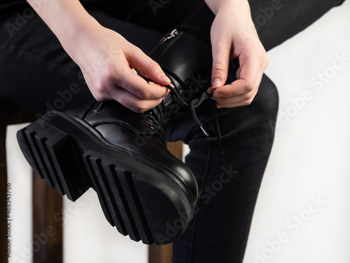 Fashionable lace-up leather boots. A young girl in black jeans is tying her shoelaces. Fashionable, stylish collection of women's shoes. Close-up.