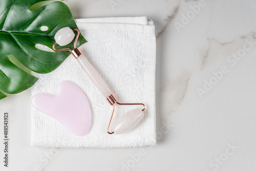 Fototapeta Naklejka Na Ścianę i Meble -  Face rollers, massager guasha scraper, made of natural quartz stone. Self-care set. homemade Spa products on a wtite towel on marble background, the concept of Spa and Wellness with space for text