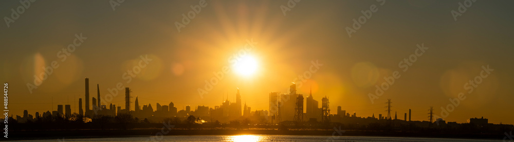 Stunning rising sun above Manhattan skyline NYC with silhouette buildings, early morning sunray filled sunrise, panoramic view and perspective.