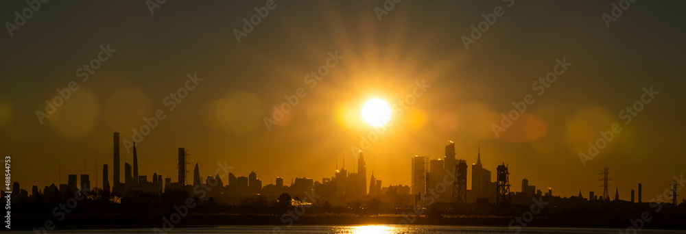 Stunning rising sun above Manhattan skyline NYC with silhouette buildings, early morning sunray filled sunrise, panoramic view and perspective.