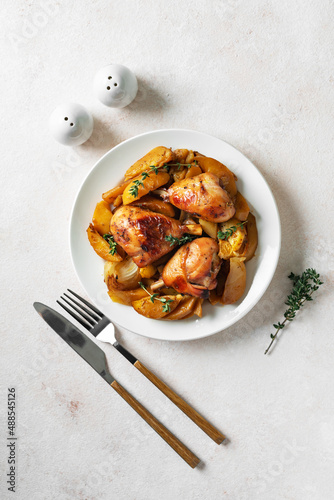 Baked chicken legs and potatoes with oranges, garlic and onions in a plate on a light culinary background