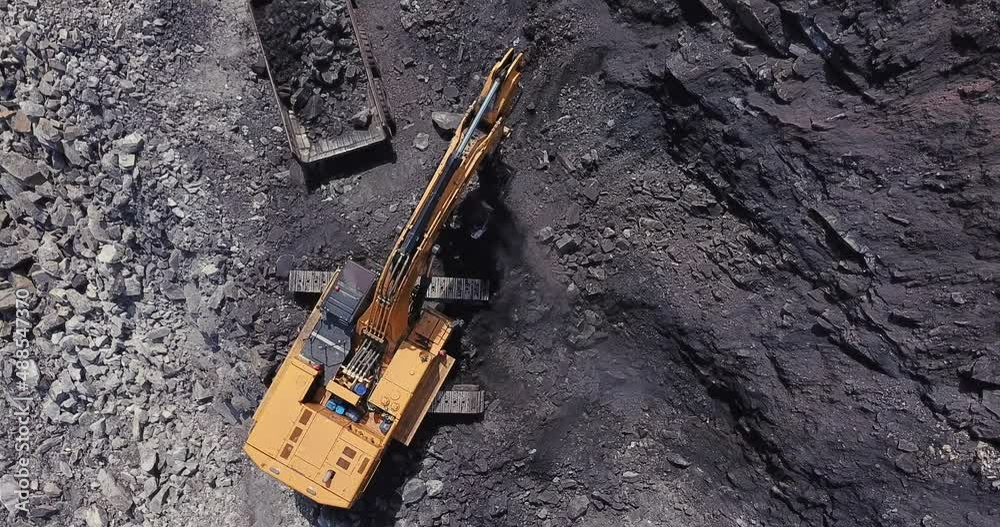 Drone view of yellow mine excavator loads coal into large dump truck at open pit coal mining area. Aerial footage of process of mining coal in a quarry. 