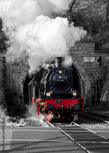 Steam train with historic locomotive and coming to light out of “Schloßberg Tunnel“ at railroad crossing in Arnsberg Sauerland Germany on Ruhr Valley line. Vintage railway scene colored engine.