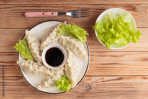 Top view of fresh boiled Chinese dumplings with soy sauce and green salad on wooden background. With copy space.