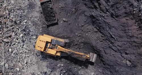 Drone view of yellow mine excavator loads coal into large dump truck at open pit coal mining area. Aerial footage of process of mining coal in a quarry. 