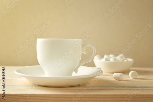 A cup of coffee on a wooden table. Next to the cup is a small plate of marshmallows