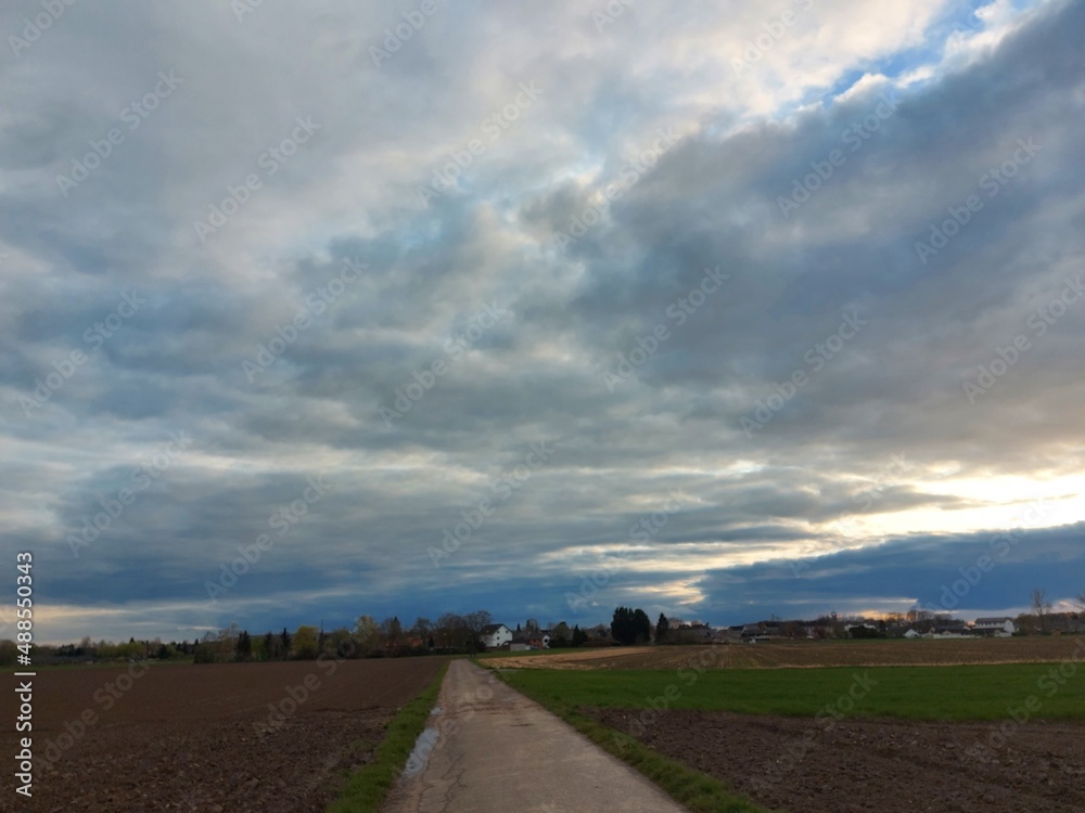 Bewölkter Himmel vor dem Sturm. Graue, schwere Wolken über dem Feld. Die Agrarlandschaft vor dem Sommerregen. Gepflügte Felder so weit das Auge reicht, bereit zur Aussaat. Eine ländliche Straße.