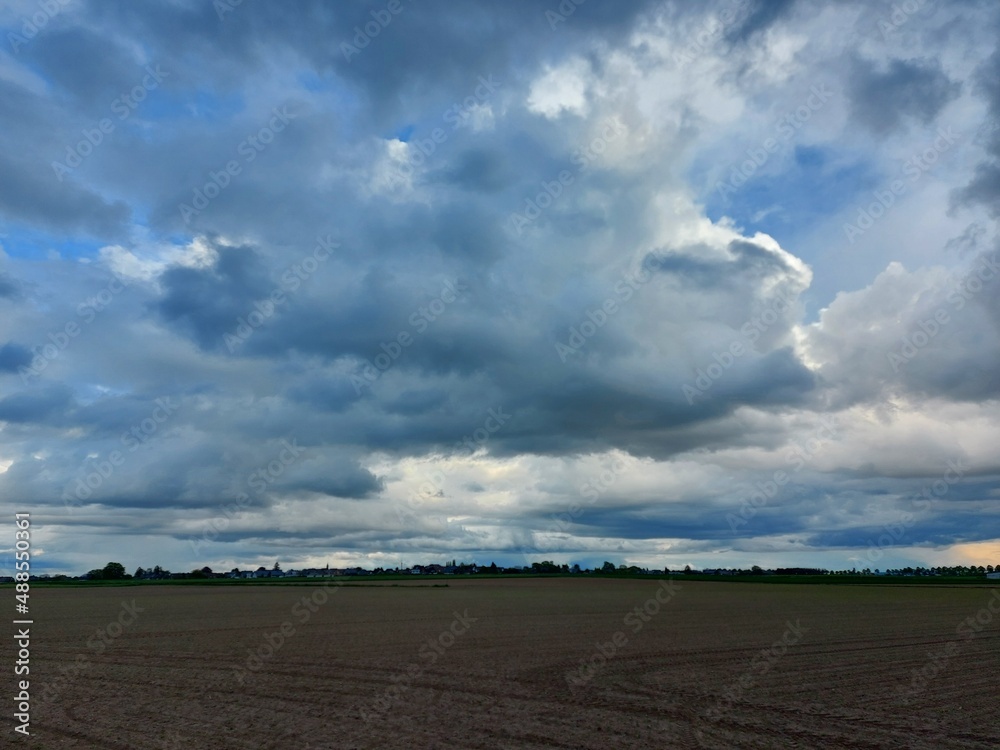 Bewölkter Himmel vor dem Sturm. Graue, schwere Wolken über dem Feld. Die Agrarlandschaft vor dem Sommerregen. Gepflügte Felder so weit das Auge reicht, bereit zur Aussaat. Eine ländliche Straße.