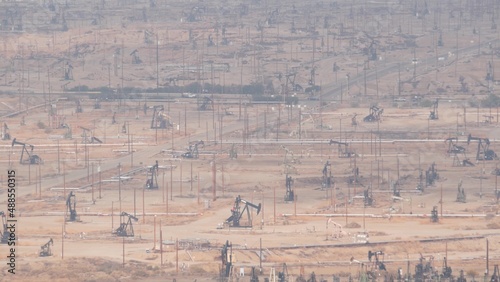 Wells with pump jacks on oil field, California USA. Rigs for crude fossil extraction working on oilfield. Industrial landscape, derricks in desert valley. Many pumpjacks platforms on oilwells pumping.