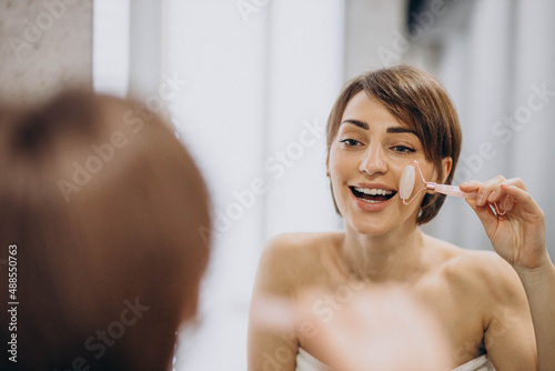 Young woman looking into the mirror and using jade face roller at home