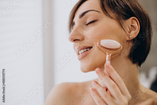 Young woman using jade face roller at home