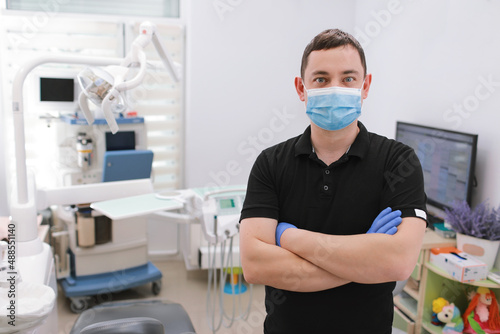A male dentist in uniform and medical face mask poses against a background of dental equipment in a dental office. Healthy teeth and medicine concept. dentist s reception