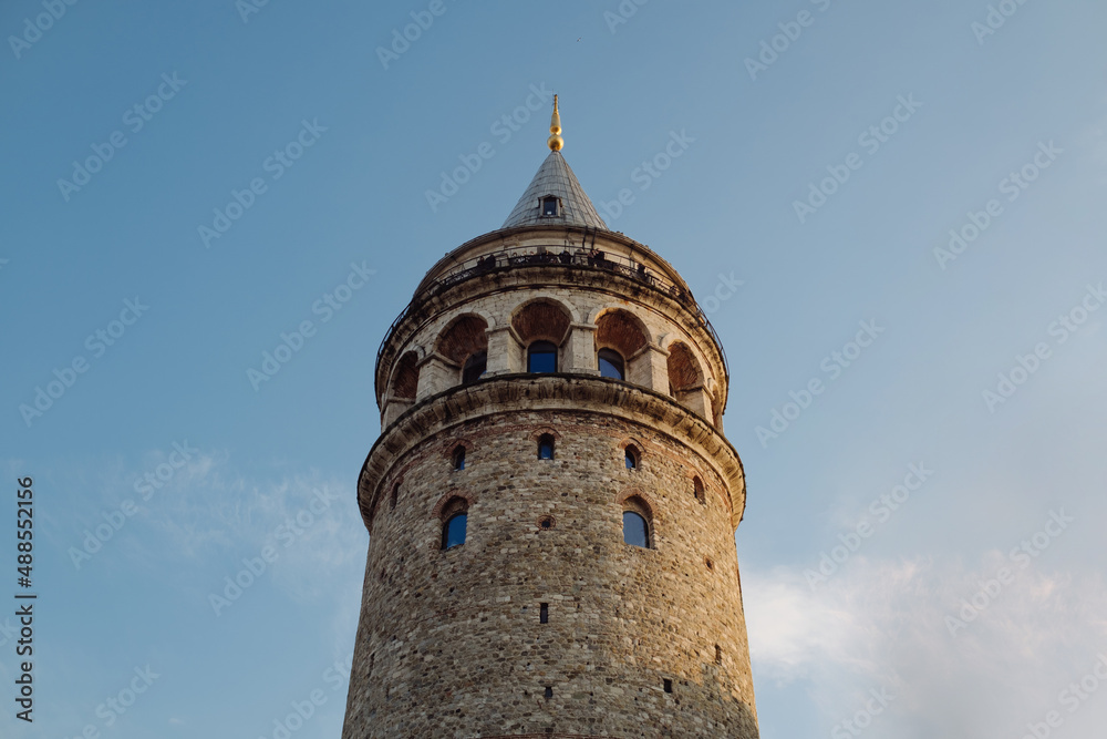Galata tower, a view of Galata Tower taken against a blue sky, visitor peoples on top of the tower are taking pictures, historical Istanbul and an architectural work that should definitely be seen.